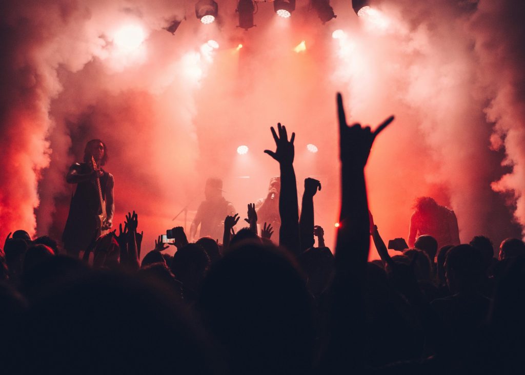 Crowd enjoying a live rock concert with band performing on stage amidst vibrant red lighting and smoke effects