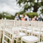 Elegant outdoor wedding setup with wooden chairs and blurred background.
